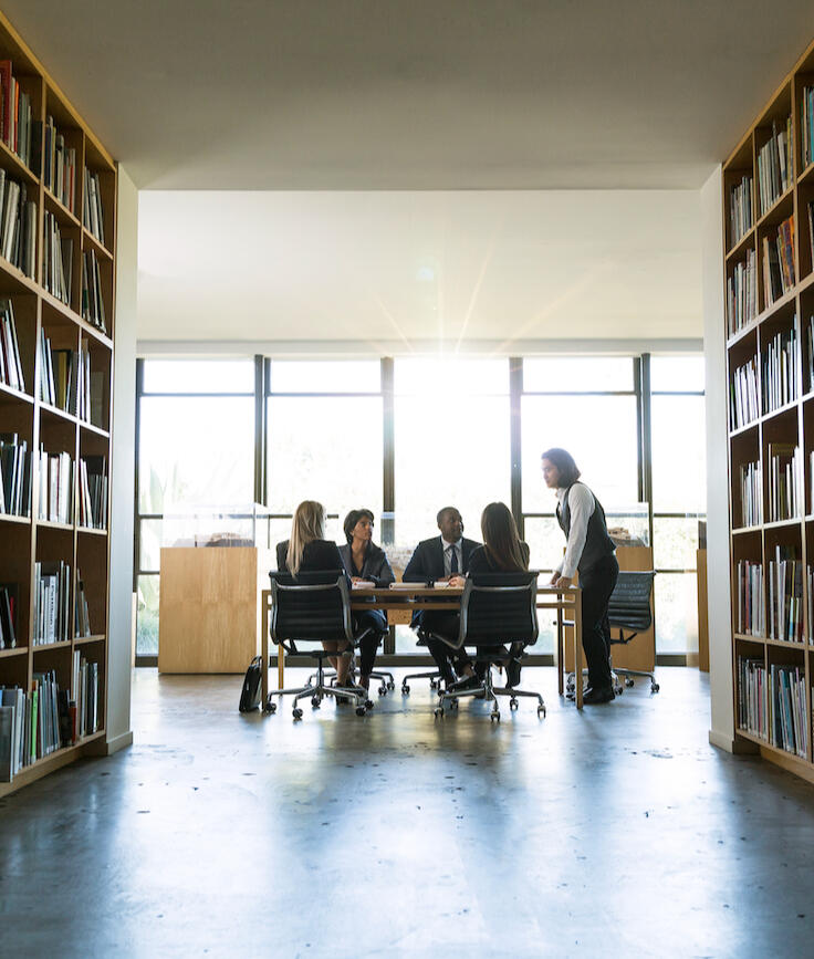 A group of people at a desk having a meeting between library shelving